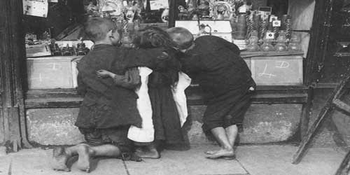 A group of Victorian children, with bare feet, look in a shop window.