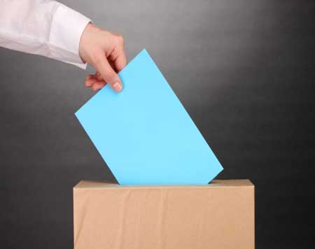A hand placing a vote into a ballot box.
